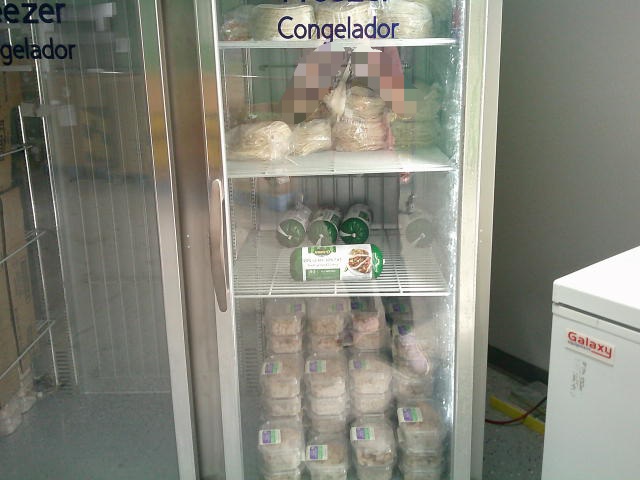 Bags of tortillas on the first and second shelf, tubs of ground turkey on the third shelf and plastic container of chicken on the bottom in a fridge.
